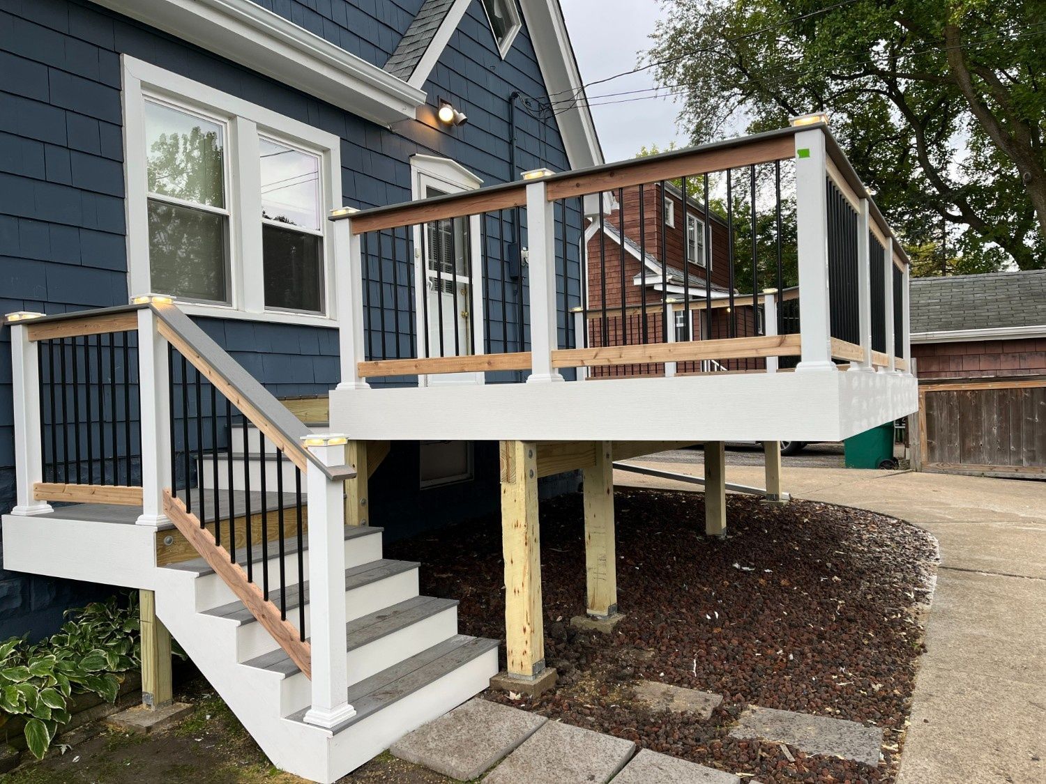 Wooden deck stairs and railing attached to a blue house in a backyard