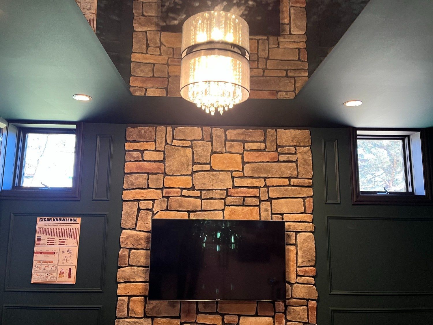 Brick fireplace wall with wall-mounted TV, chandelier, and dark green paneled walls inside a room