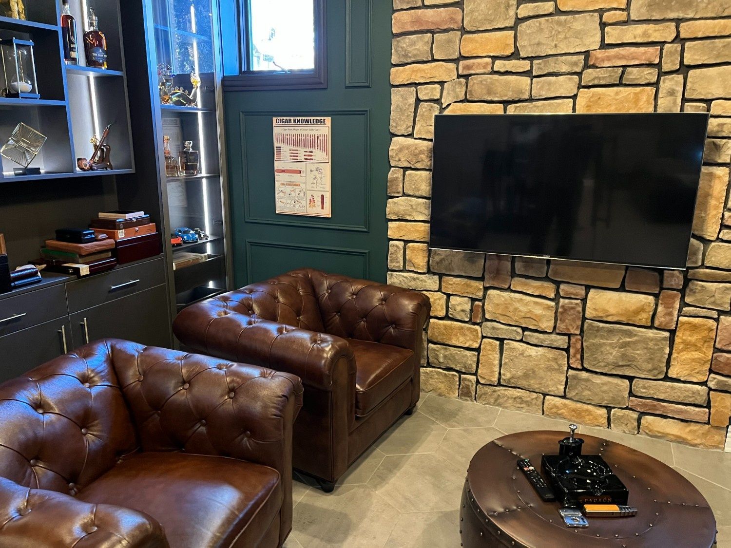 Cozy lounge with leather chairs, stone fireplace wall, wall-mounted TV, and a round coffee table