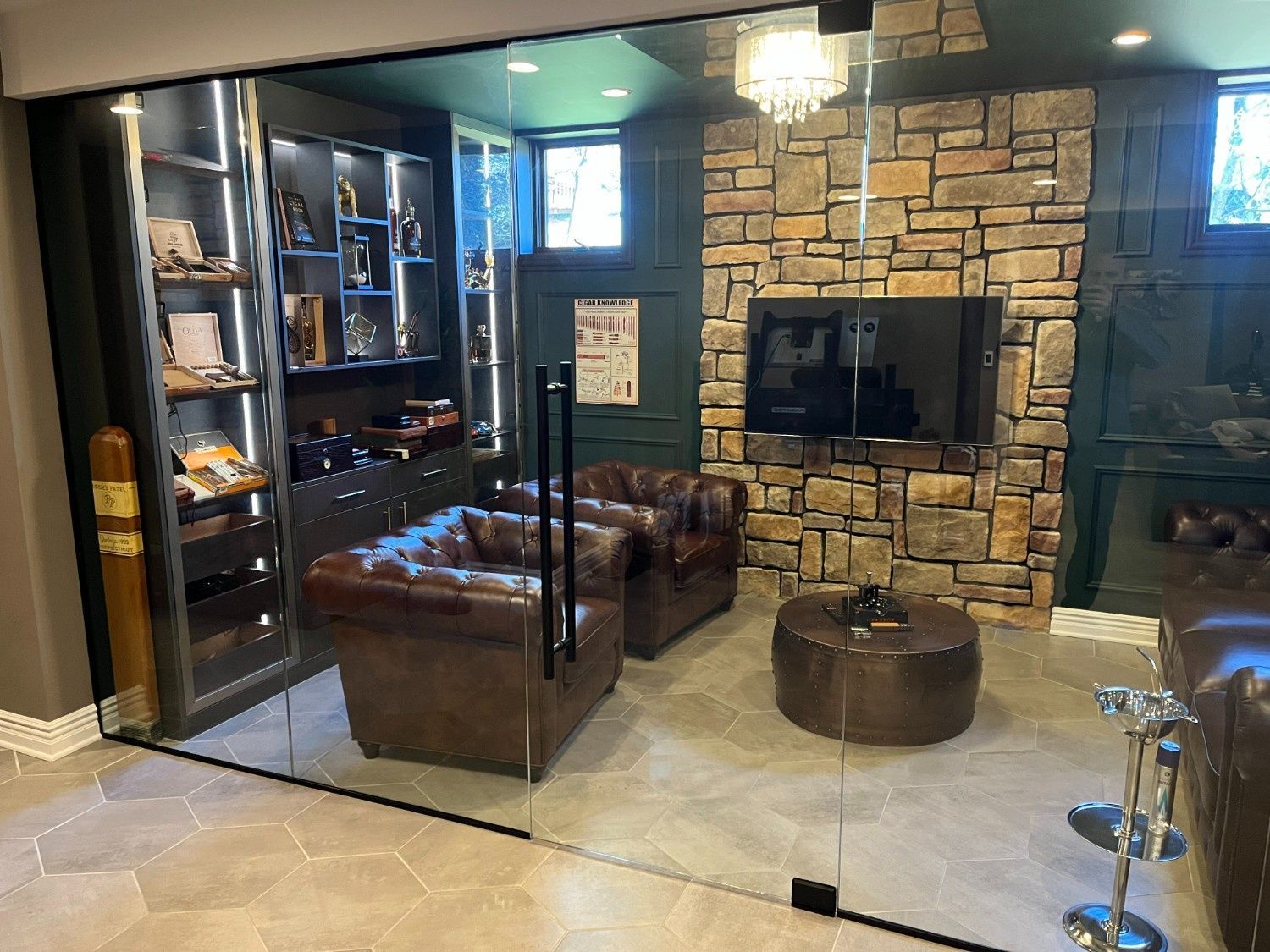 Modern living room with stone fireplace, leather chairs, glass partition, and beige tile floor