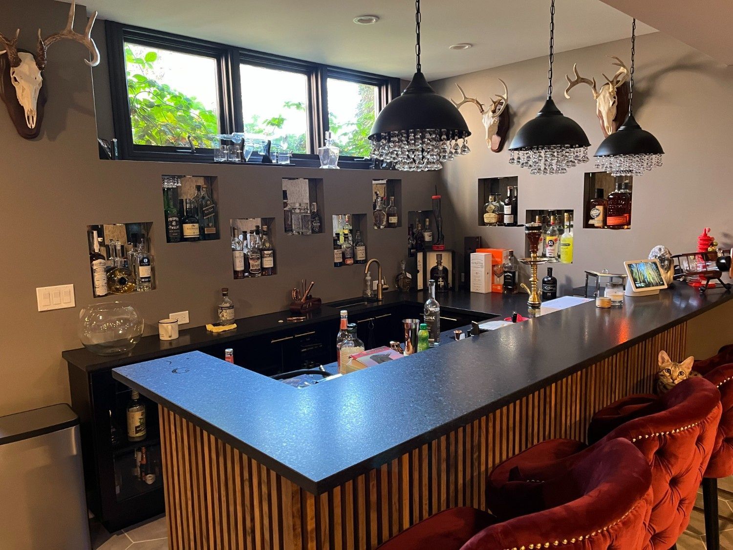 Dim modern bar interior with black pendant lights, blue counter, and red stools
