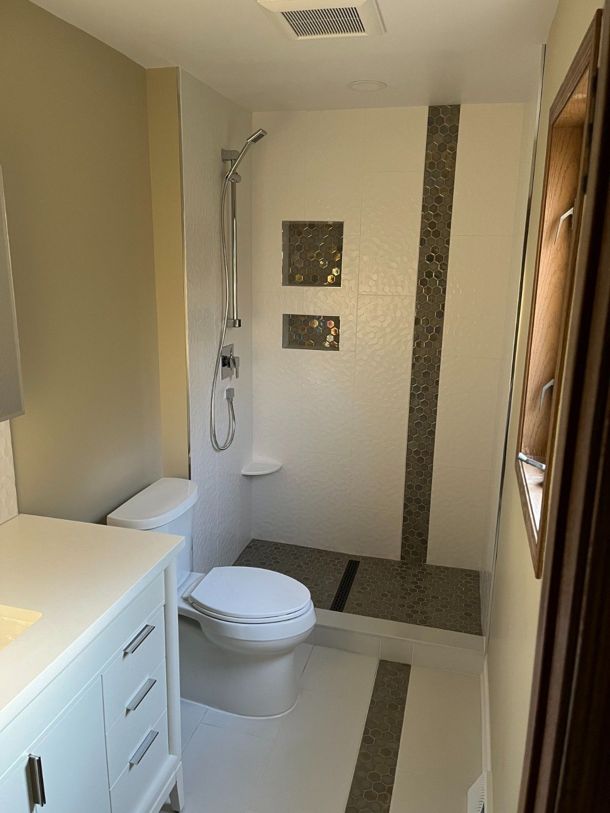 Small modern bathroom with white toilet, vanity, and walk-in shower with gray tile accents.