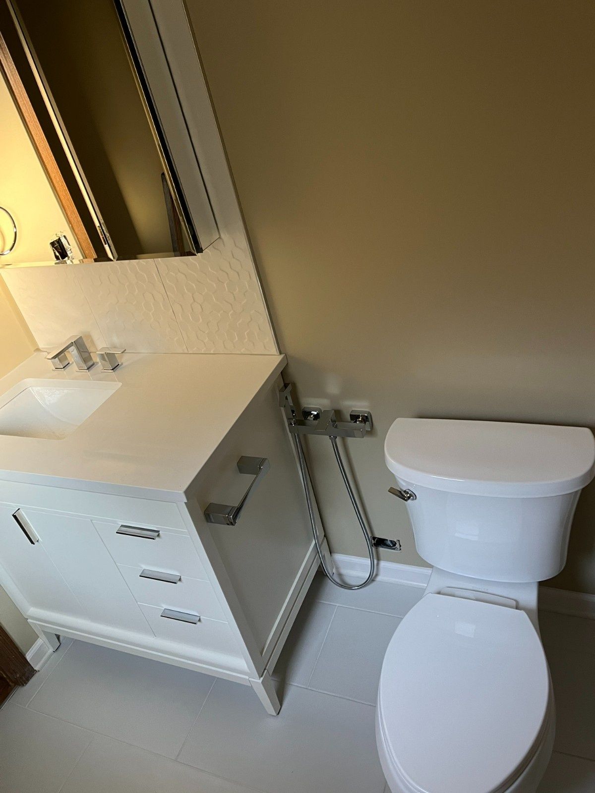 Small bathroom with toilet, sink vanity, mirror, and wall-mounted showerhead in beige tones