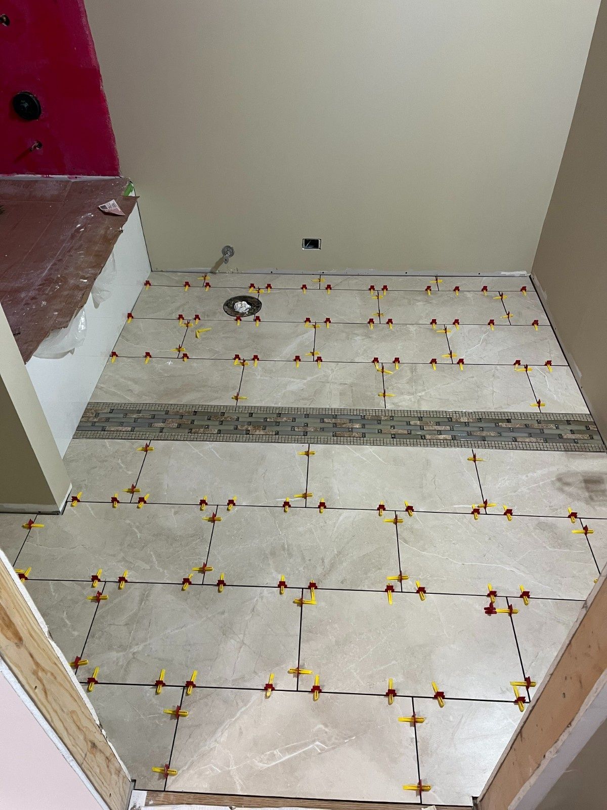 Partially tiled room floor with white tiles, yellow spacers, and a pink wall in the corner