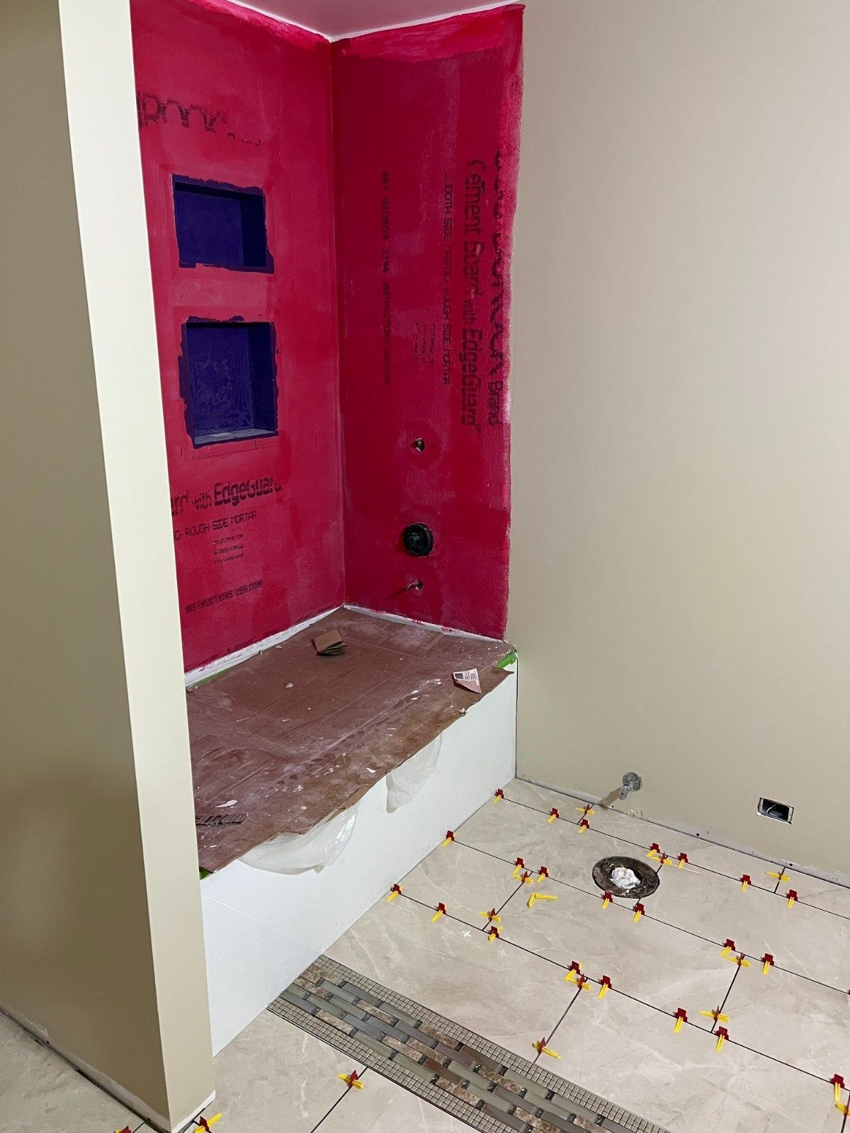 Pink tiled shower alcove with two blue niches and a raised step beside white floor tiles