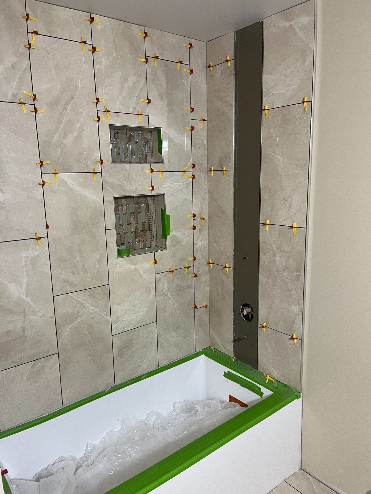 Bathroom under renovation with tiled walls and a bathtub covered in protective wrap