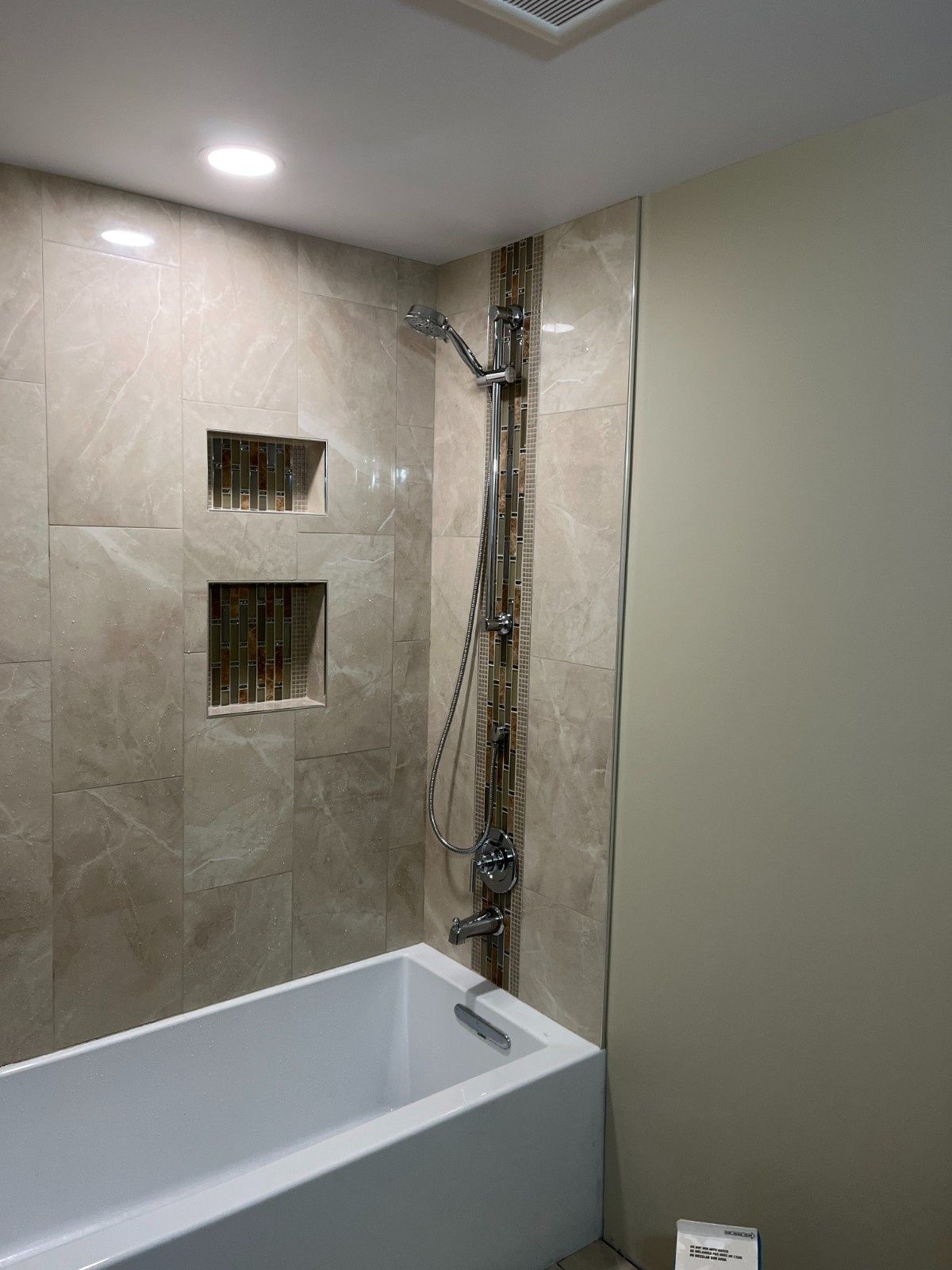 Modern bathroom with a white bathtub, tiled shower wall, and exposed shower fixtures unfinished on the right.