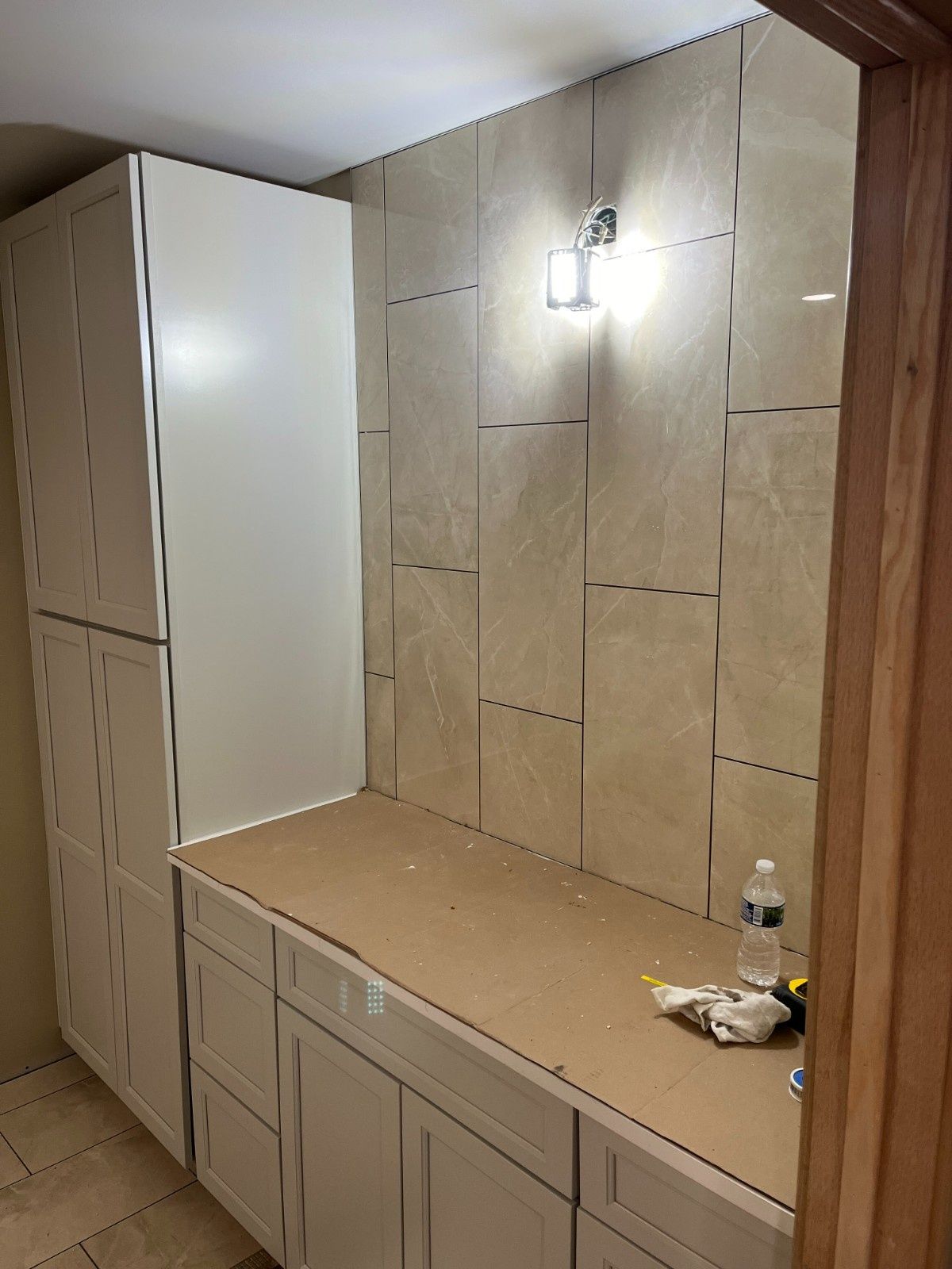 Built-in cabinets and bench in a tiled hallway with a wall light and a small bottle on the counter.