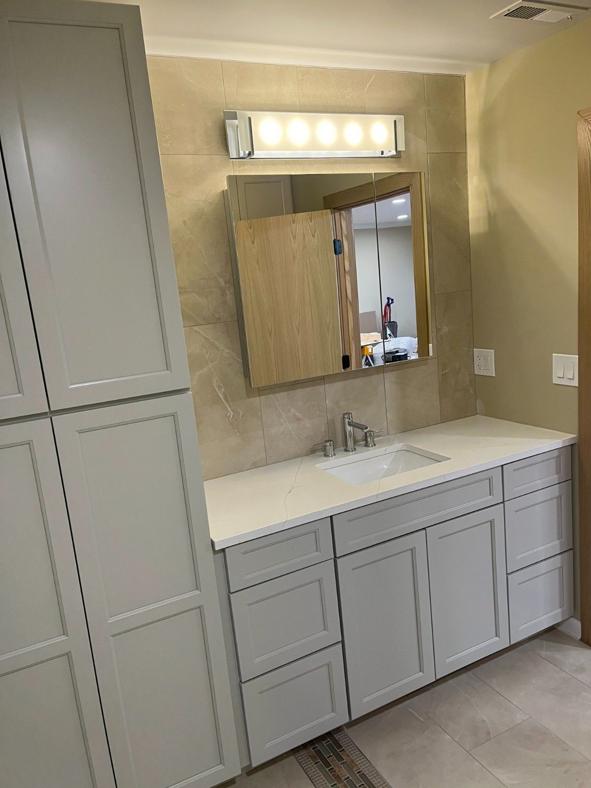 Bathroom vanity with white cabinets, rectangular mirror, and light fixture above a sink against beige walls.