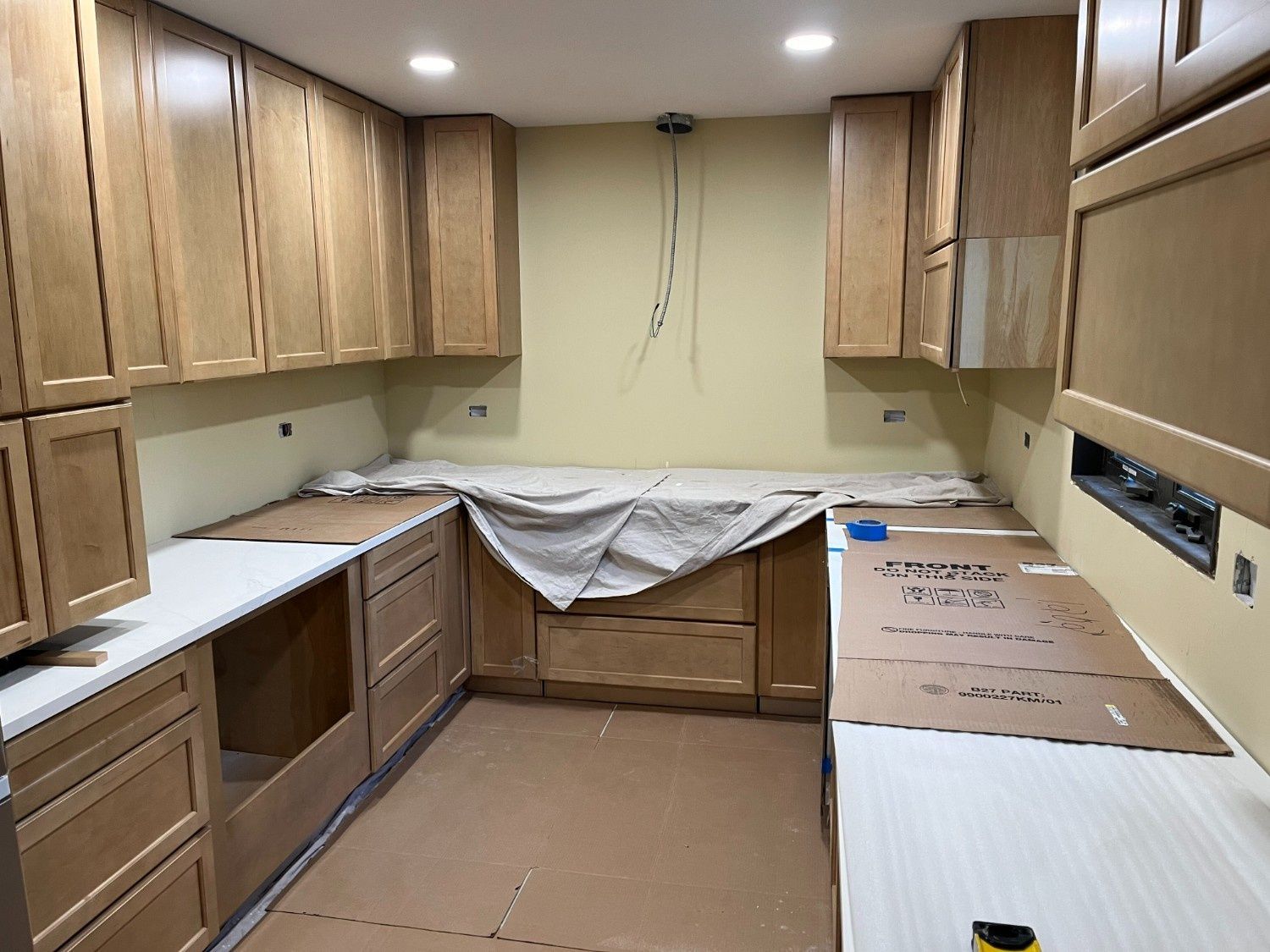 Unfinished kitchen with wood cabinets, white counters, and cardboard protecting the floor during renovation