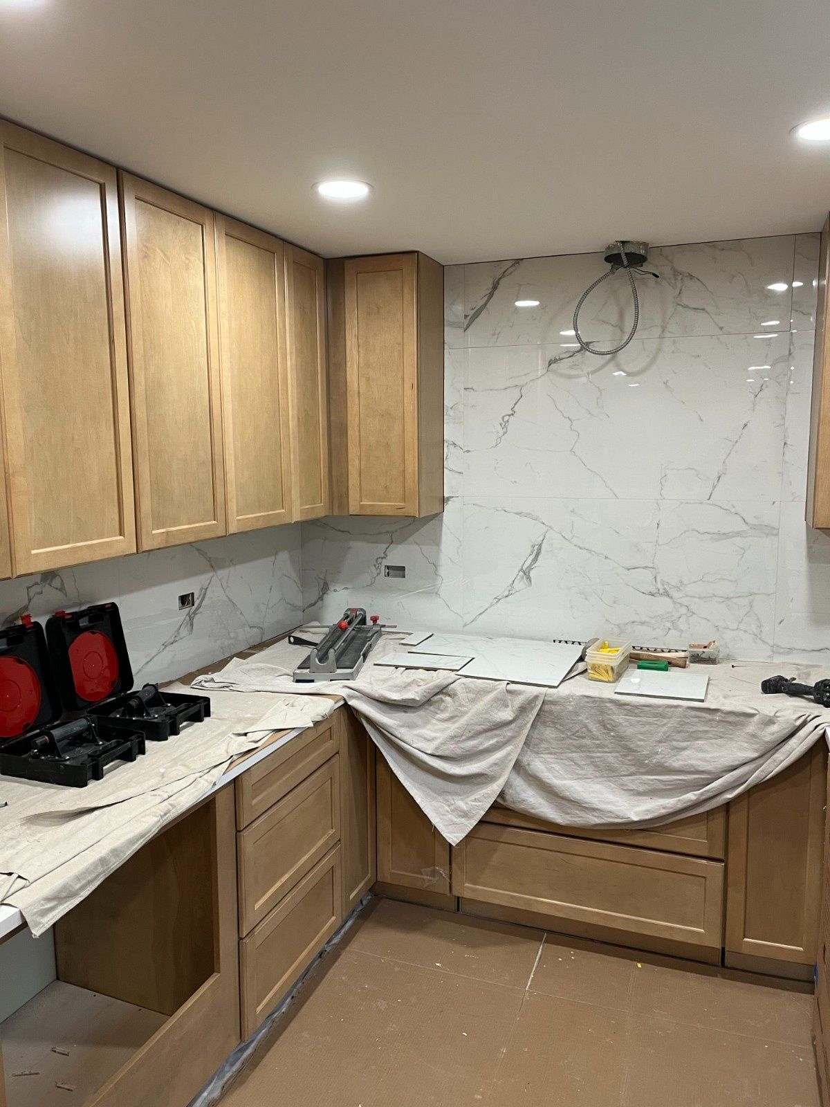 Small kitchen under renovation with wooden cabinets, marble-look backsplash, and tools on the countertop.