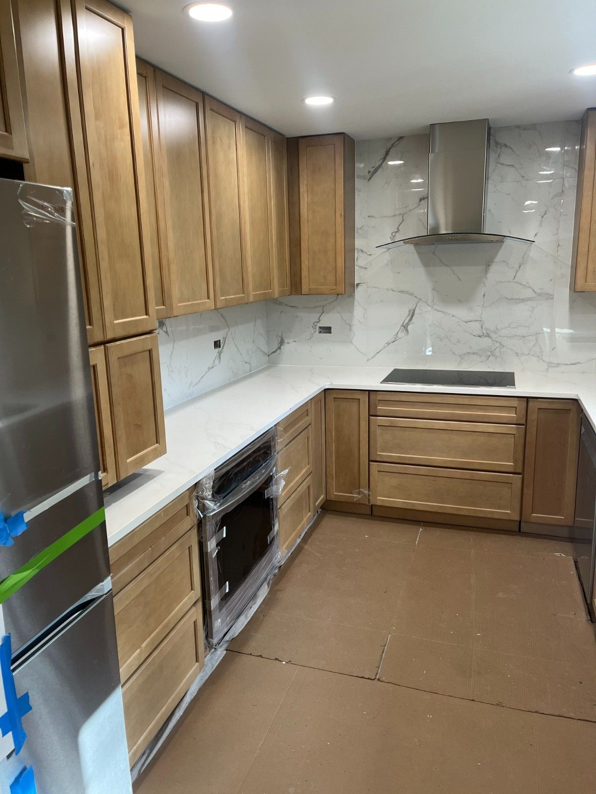 Modern kitchen with wood cabinets, stainless steel appliances, white backsplash, and brown floor coverings