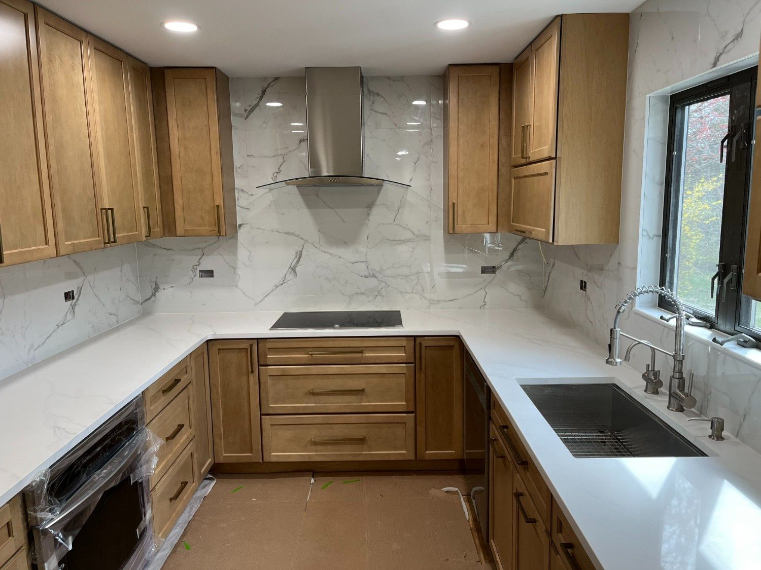 Modern kitchen with light wood cabinets, white countertops, marble backsplash, and stainless steel appliances