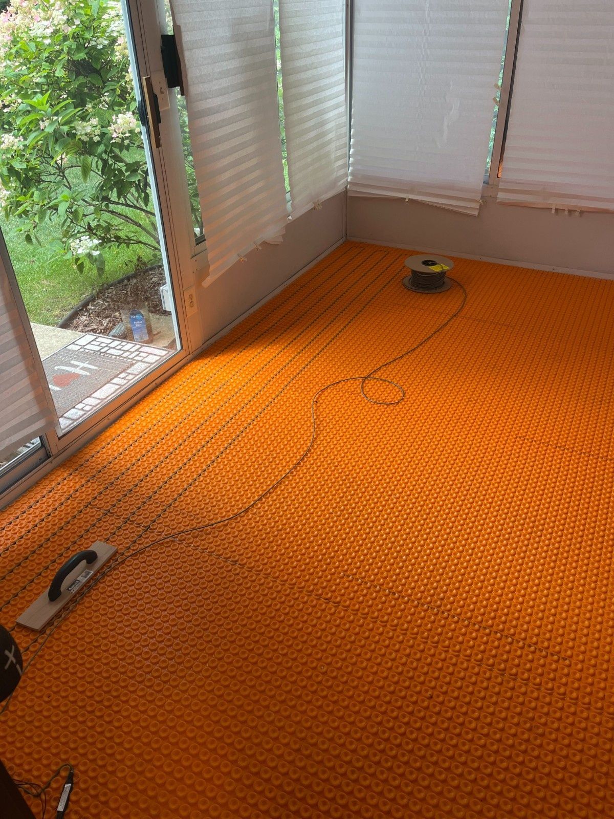 Orange carpeted room with window blinds, power cords, and a small black device on the floor.