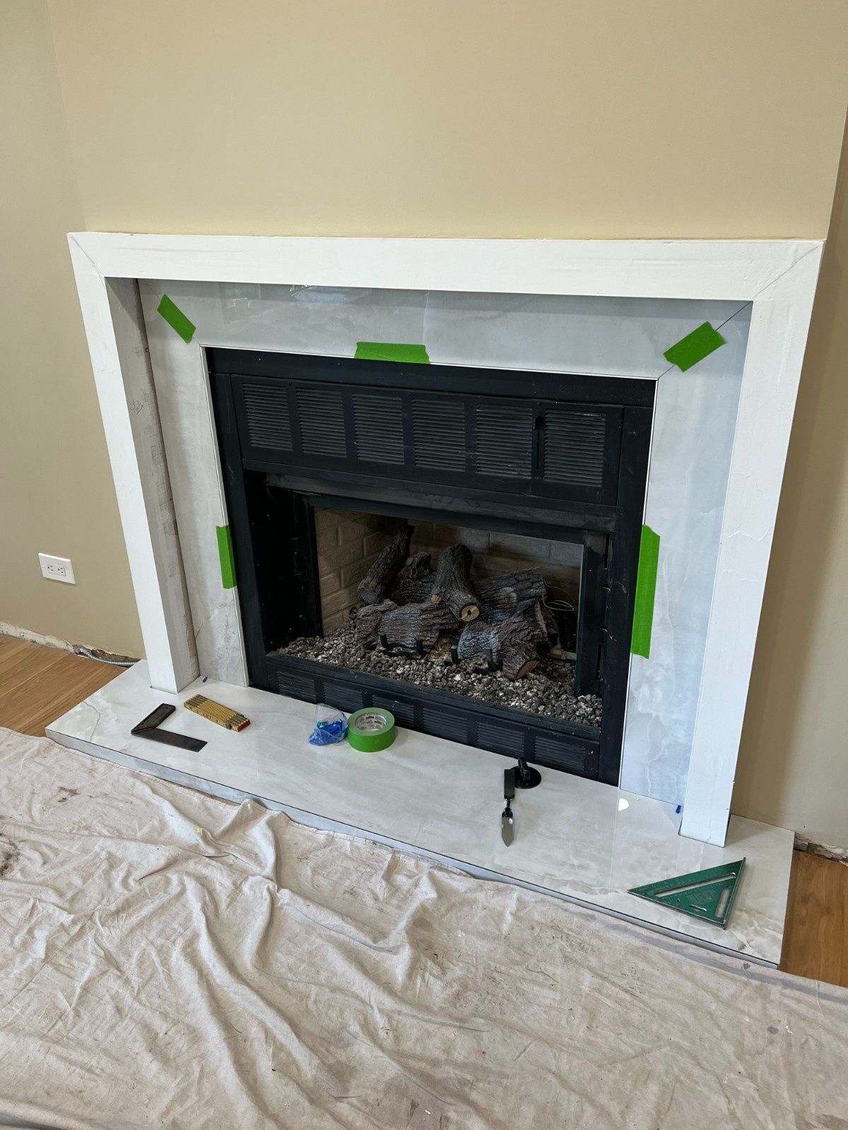 Partially painted white fireplace surround in a room under renovation, with drop cloths and tools on the floor