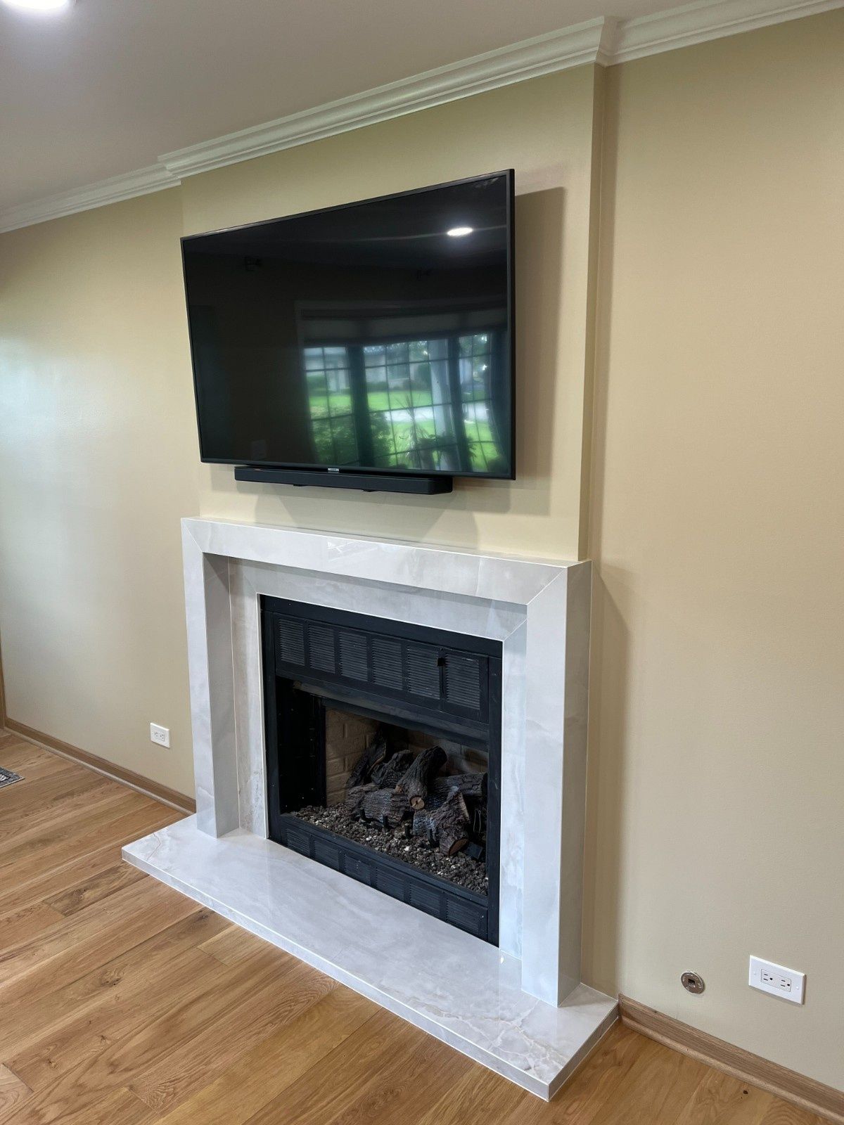Living room fireplace with a wall-mounted TV above a white mantel and hardwood floors