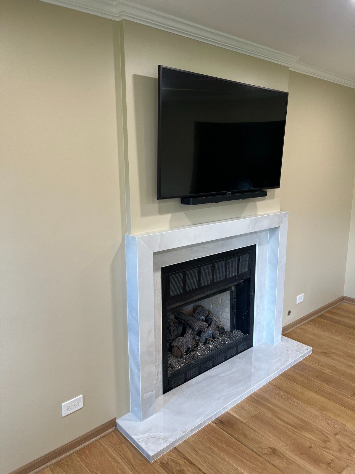 Wall-mounted TV above a white marble fireplace in a beige room with hardwood floors.