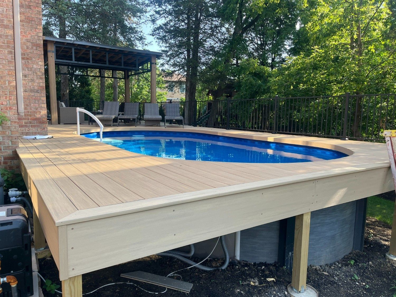 Backyard deck with an in-ground pool and covered patio beside a brick house