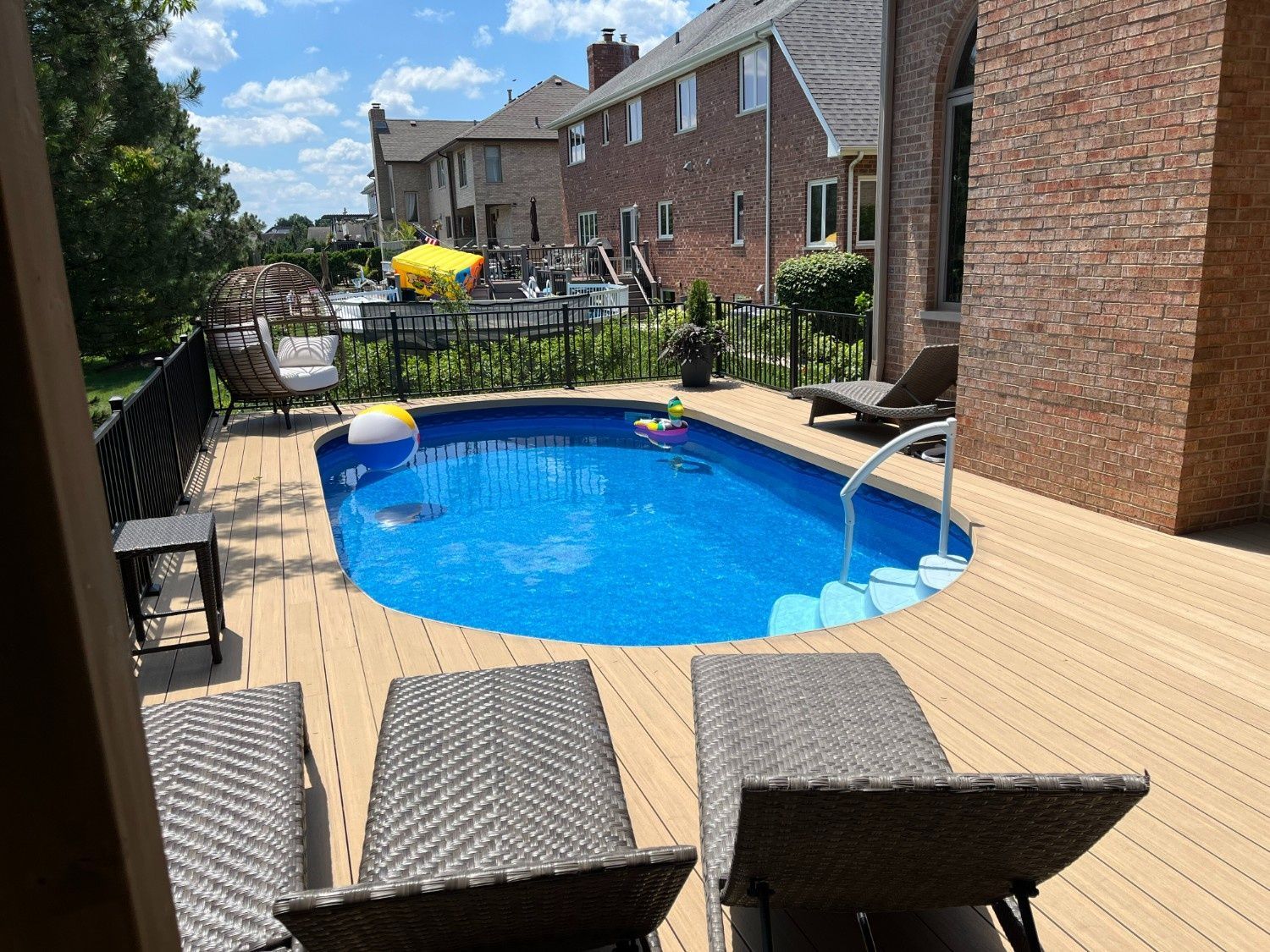 Backyard deck with a small blue swimming pool, lounge chairs, and brick houses in the background