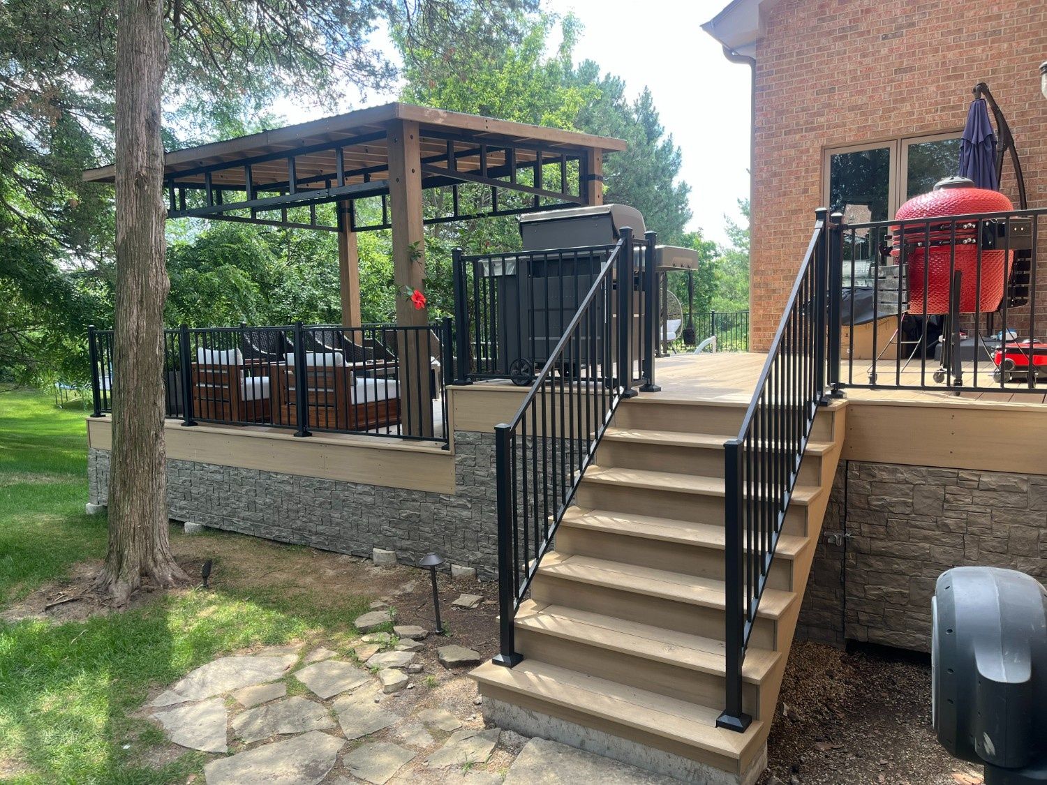 Outdoor patio with steps, black railings, pergola, and red grill beside a brick building