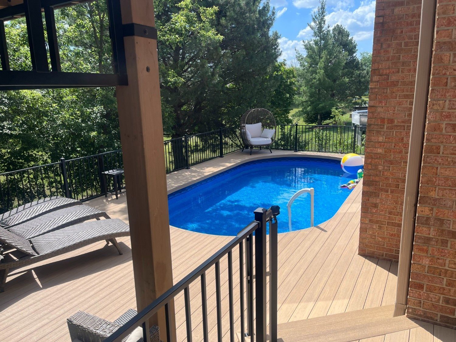 Backyard patio with a blue swimming pool, lounge chair, and brick house