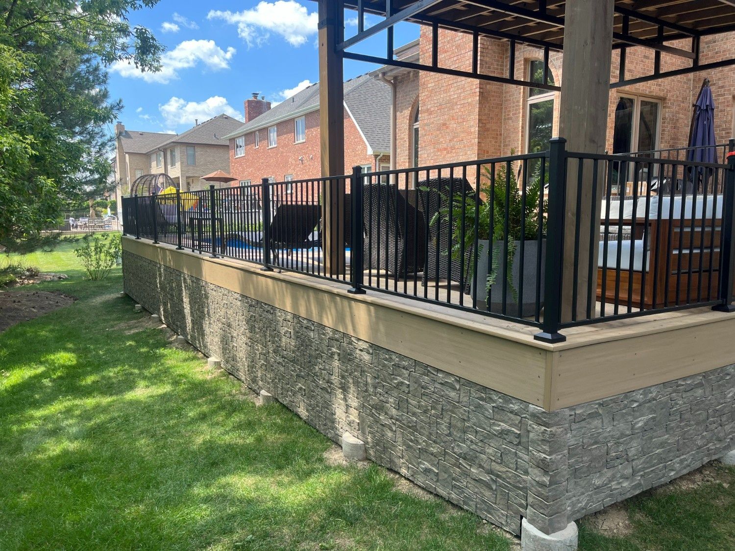 Outdoor patio with black metal railing, stone wall, and brick row houses along a grassy yard