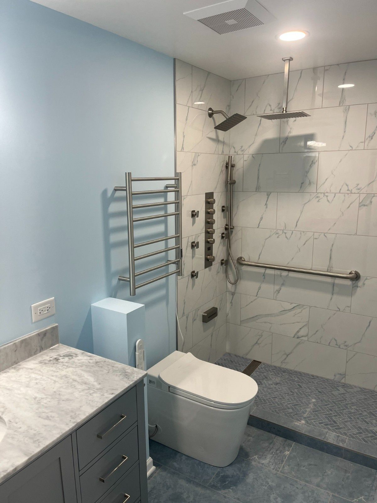 Modern bathroom with walk-in shower, toilet, sink, towel rack, and light blue wall