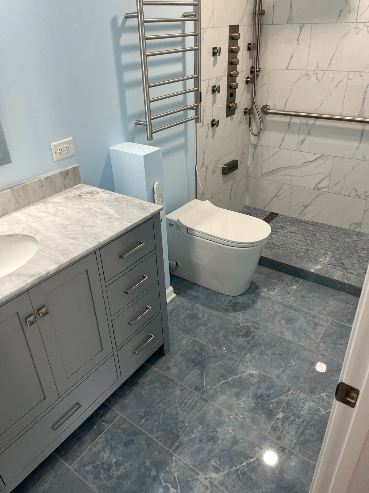 Modern blue bathroom with marble vanity, toilet, towel warmer, and walk-in shower.