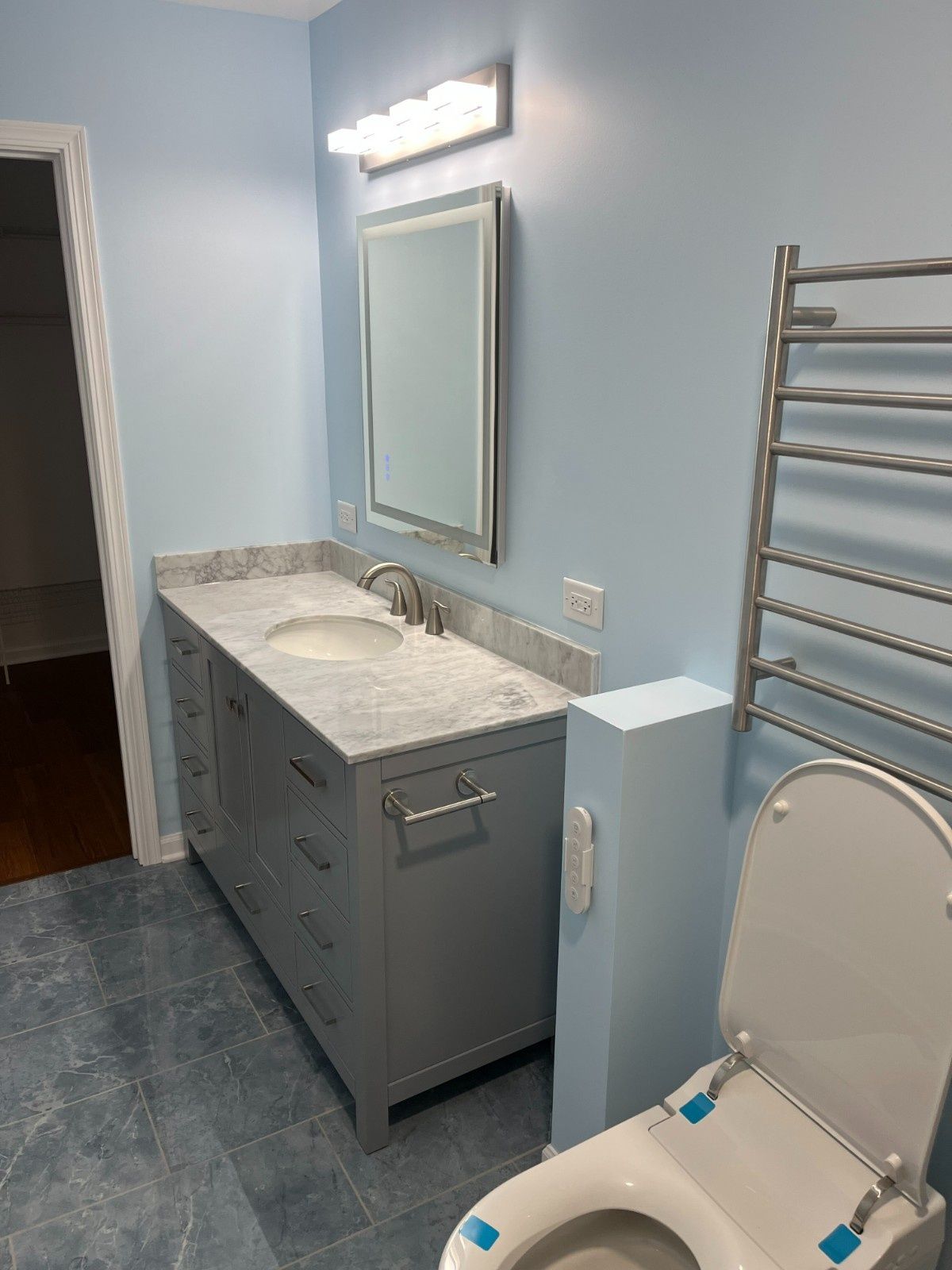 Accessible bathroom with blue walls, vanity sink, mirror, toilet, and towel warmer rack