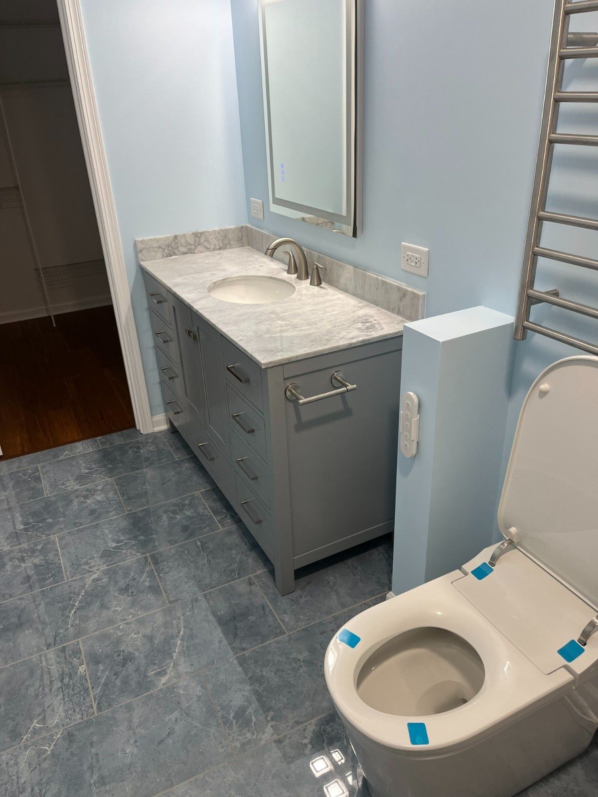 Accessible bathroom with gray vanity, mirror, and wall-mounted toilet beside a blue grab bar.
