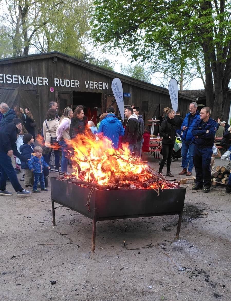 Vor dem Vereinsheim des Eisenauer Ruder Vereins brennt in einer Feuerschale ein Lagerfeuer, umringt von einer Menschenmenge.
