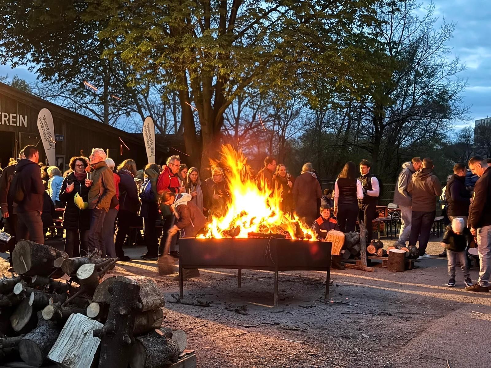 Eine Gruppe von Menschen steht nachts um ein großes Feuer herum.