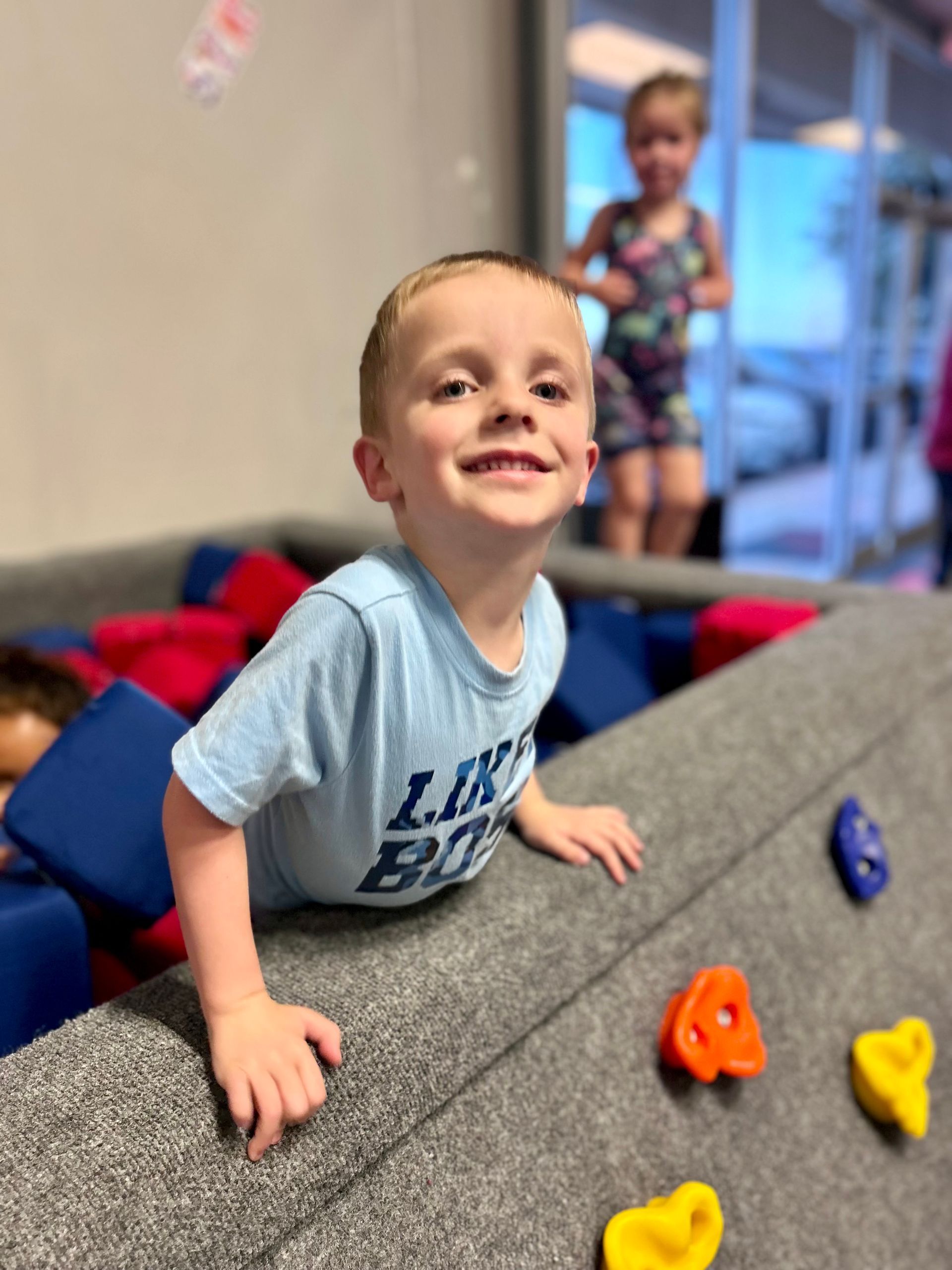 A young boy is crawling on a balance beam in a gym.
