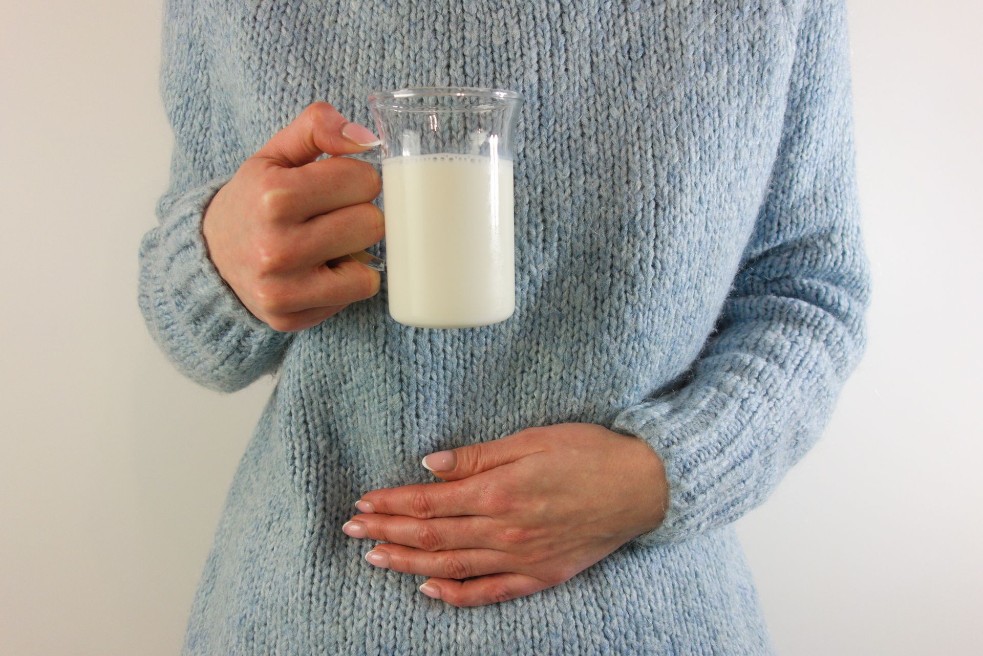 Una donna con un maglione blu tiene in mano un bicchiere di latte.