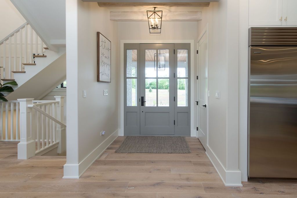 Hallway with gray front door, light wood floors, and staircase.