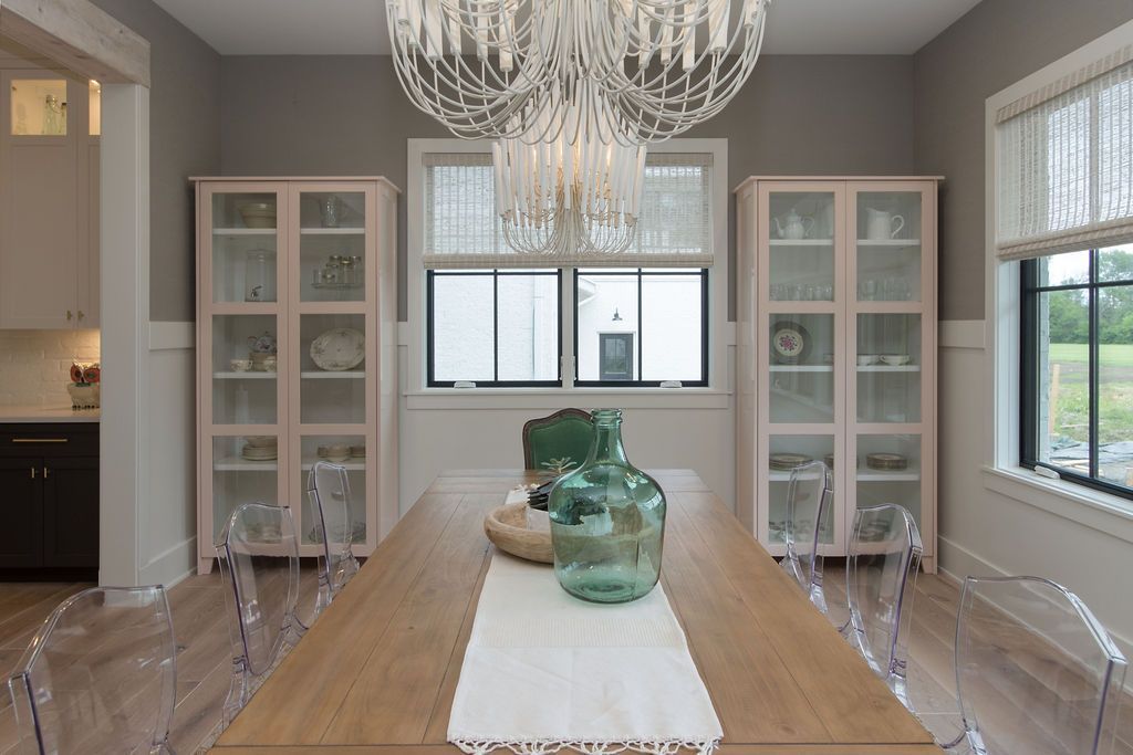 Dining room with wooden table, clear chairs, pink cabinets, and a decorative chandelier.