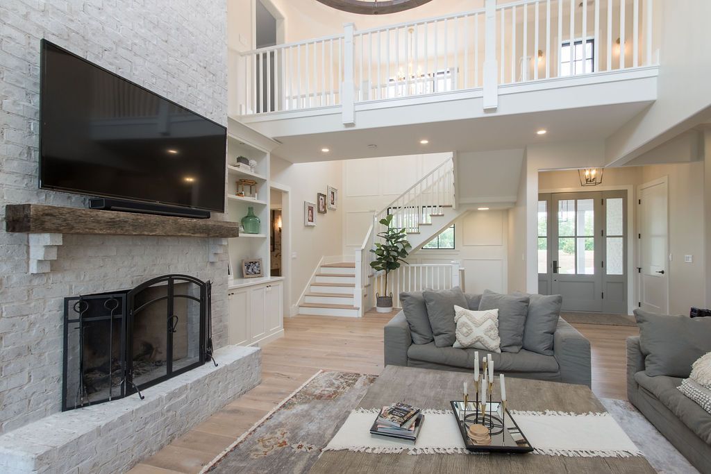 Spacious living room with fireplace, TV, staircase, and sofas. Bright, open space with neutral colors.