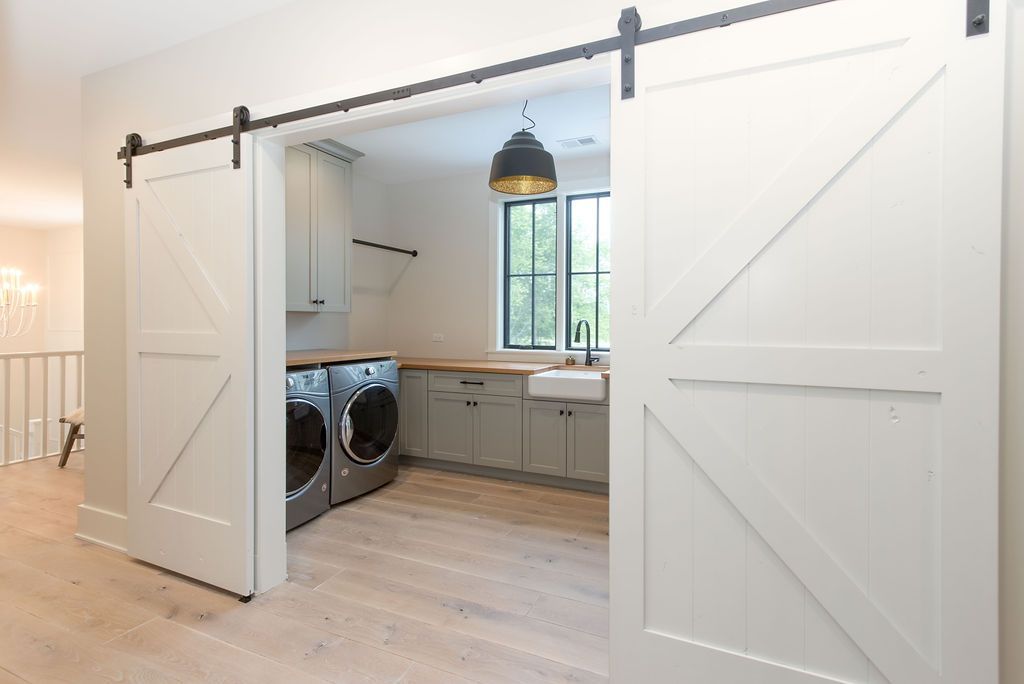 White barn doors open to a laundry room with washer, dryer, sink, cabinets, and wood countertop.
