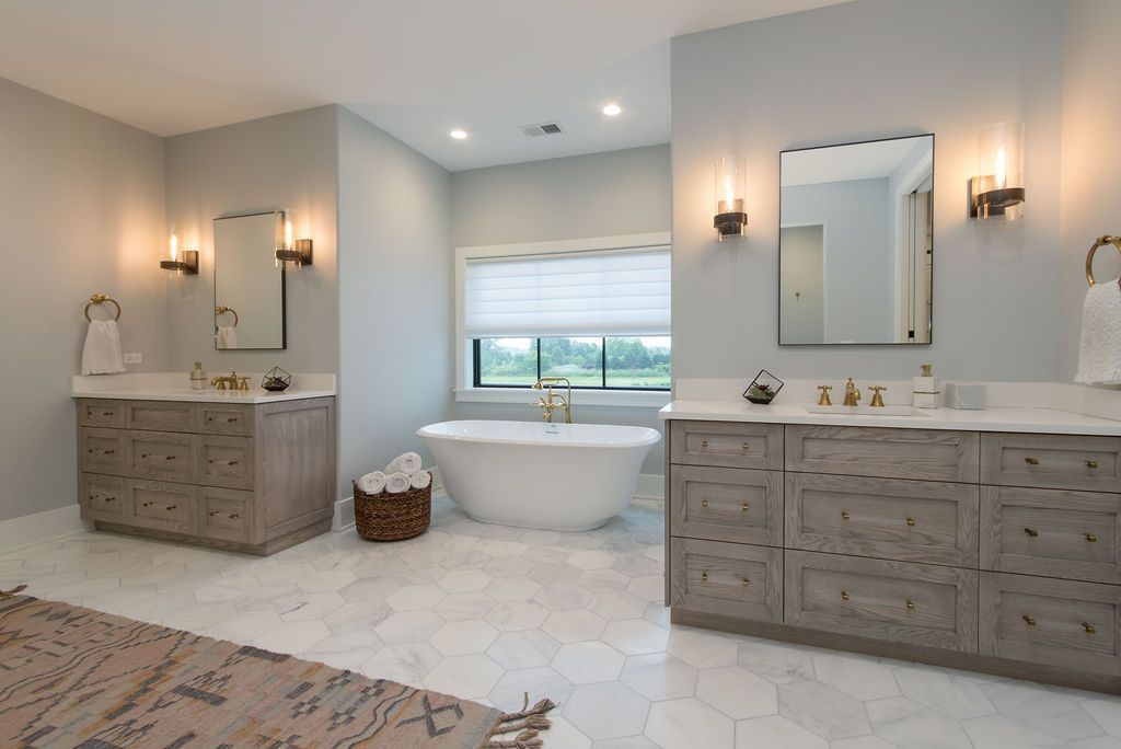 Spacious master bathroom with light gray walls, white soaking tub, and dual vanities with gold accents.