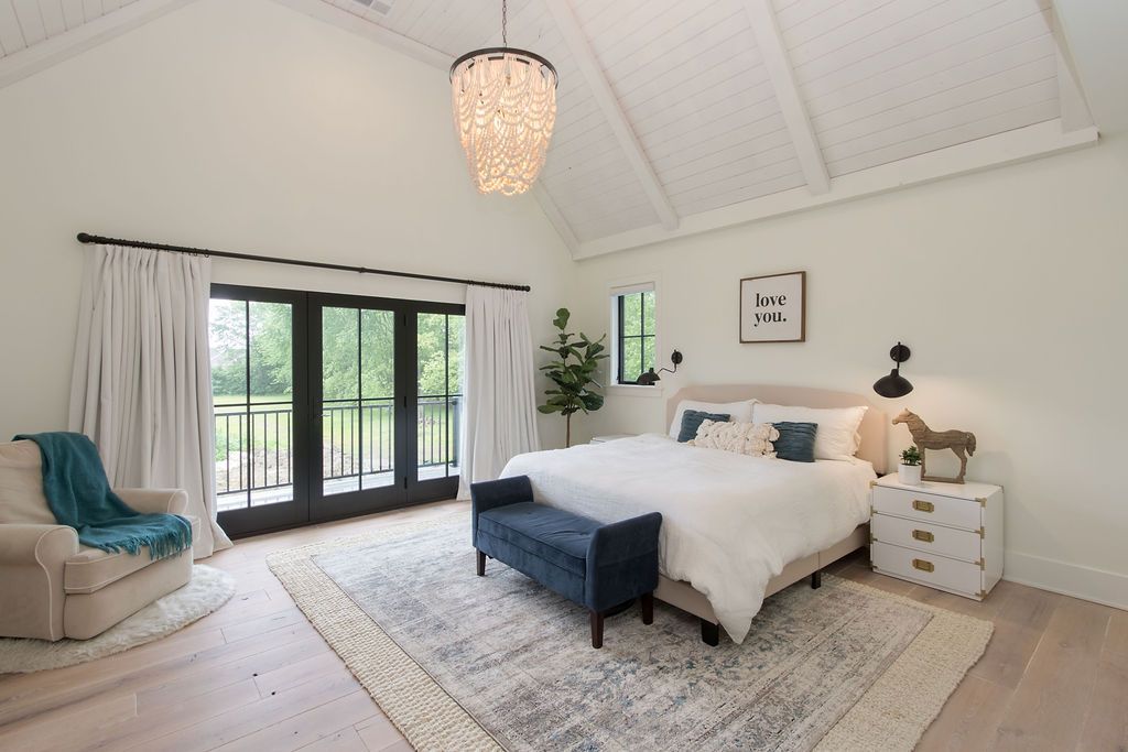 Bedroom with vaulted ceiling, white walls, and dark framed doors leading to a balcony.