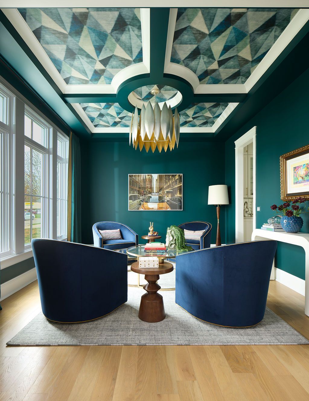 Teal-painted room with geometric ceiling design, blue armchairs, and a decorative chandelier.