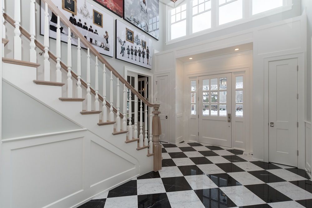 Elegant foyer with checkered floor, white walls, staircase, and framed photos.