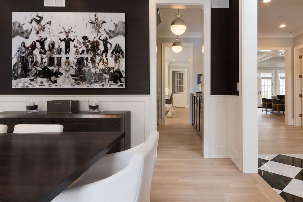 Dining room with dark table, white chairs, artwork, and hallway.
