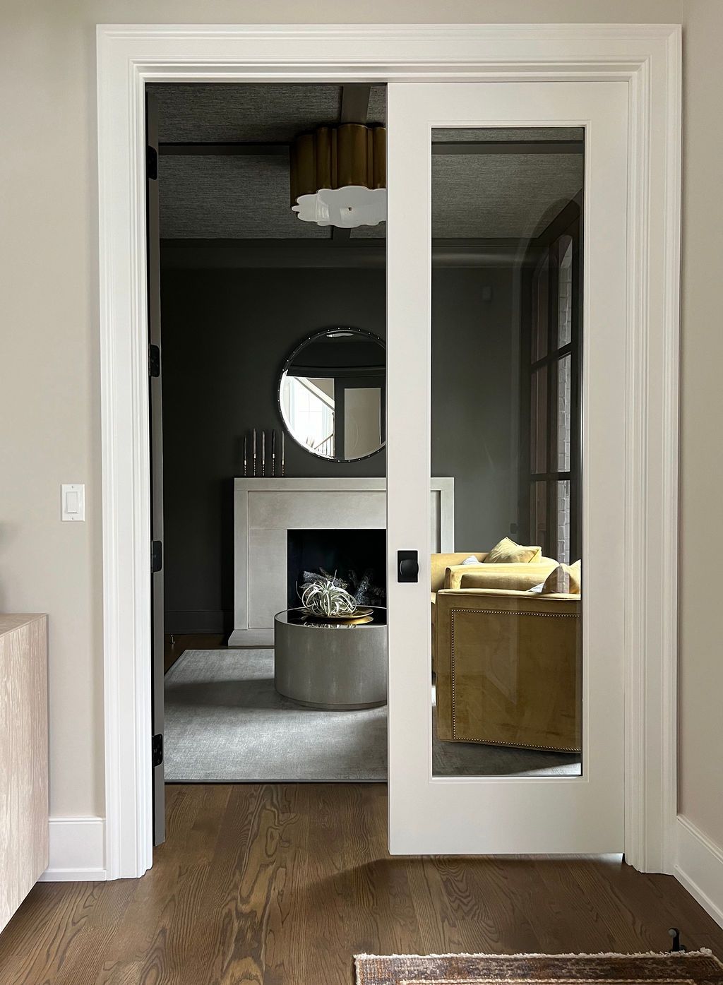 White framed glass pocket door open, revealing a living room with a fireplace, mirror, and sofa.