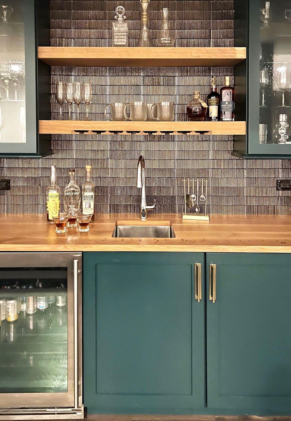 Bar area with teal cabinets, wooden countertop, shelving, and mirrored backsplash.