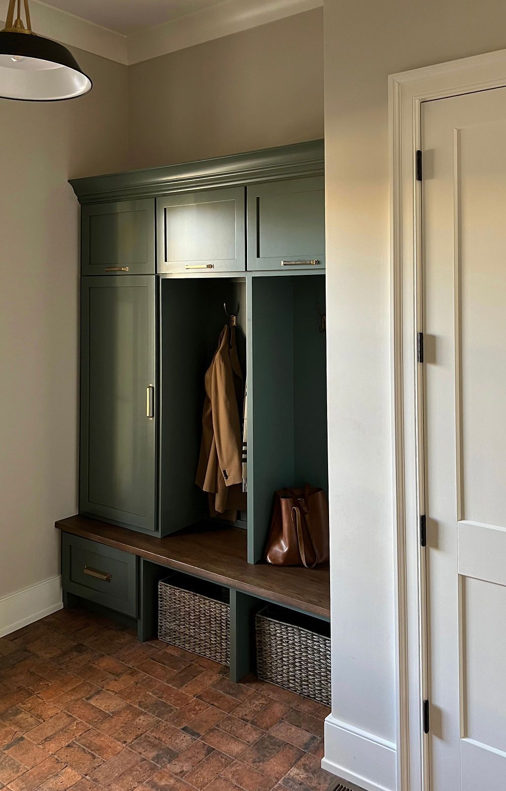 Green built-in entryway storage with hooks, cabinets, drawers, and baskets. Cork flooring and white door.