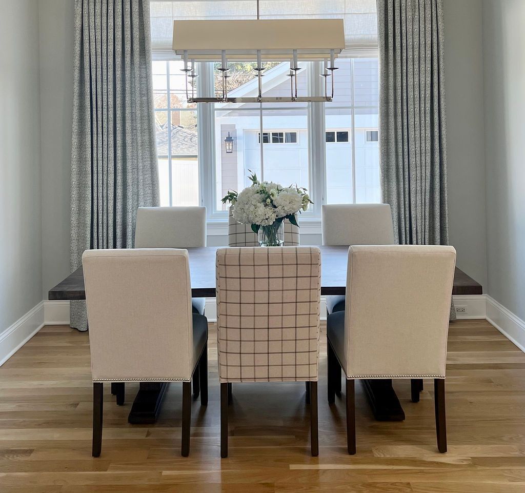 Dining room with table, chairs, flowers, and window with curtains.