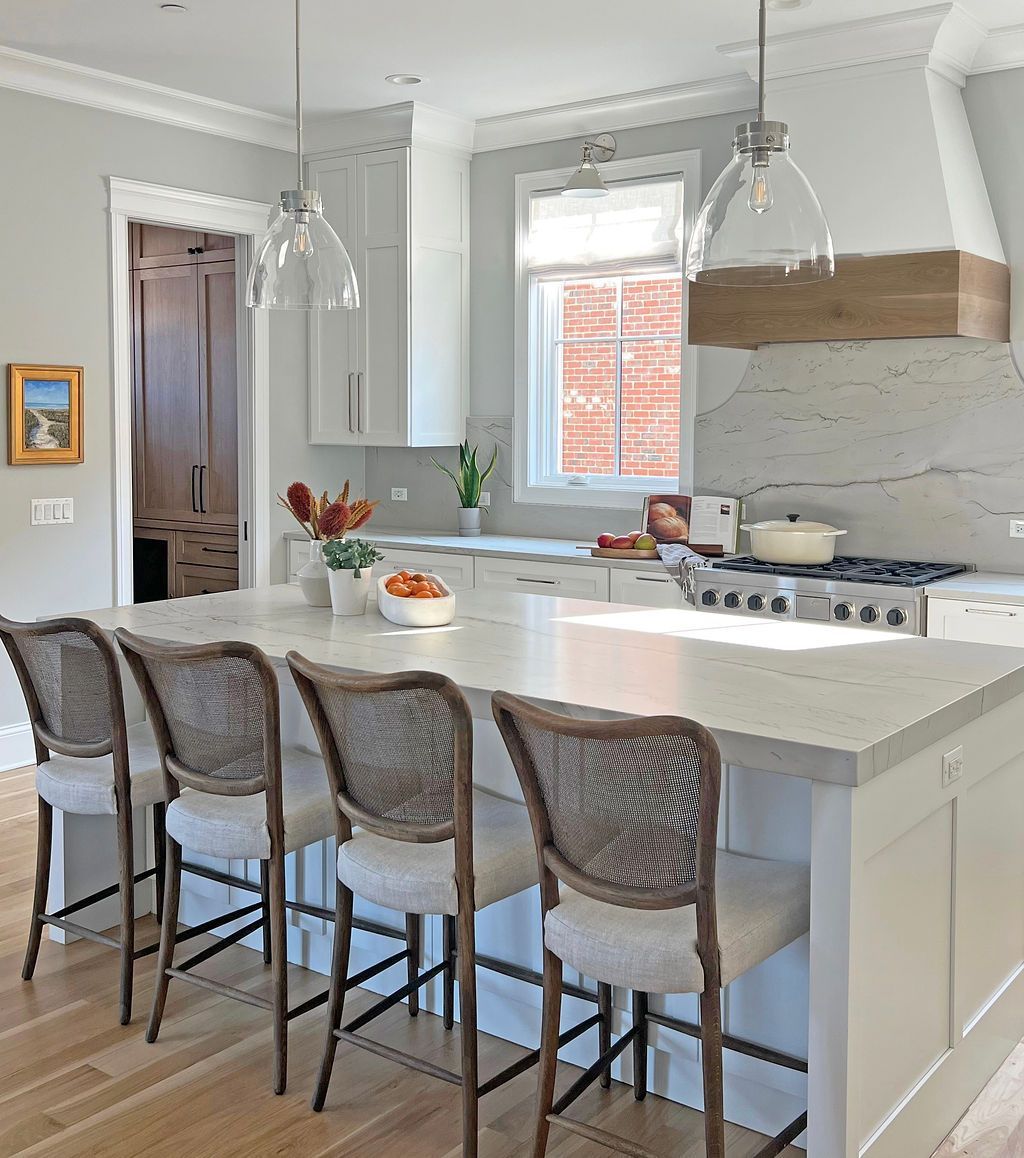 Bright kitchen with island, seating, and overhead pendant lights. Light grey cabinetry and countertops.