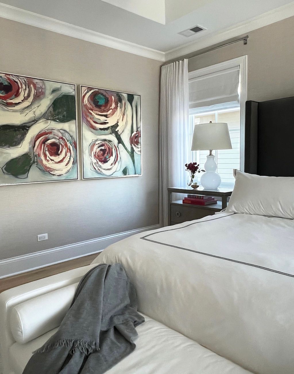 Bedroom with abstract floral art above bed, white bedding, window with sheer curtain, and white bench.