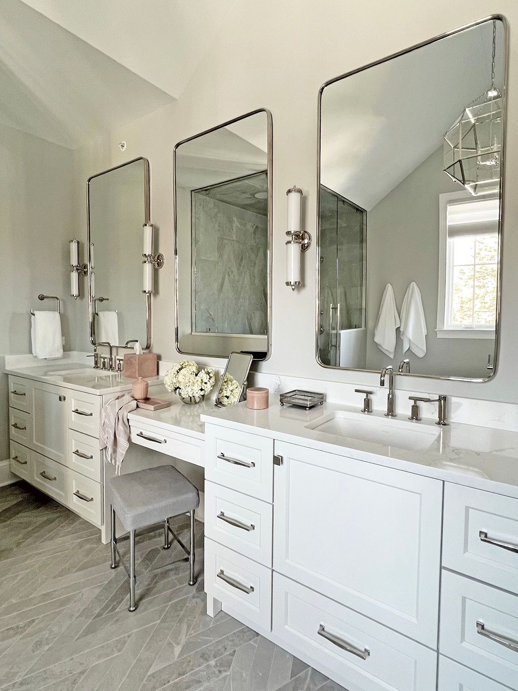 White bathroom with three mirrors, vanities, and a gray stone floor.